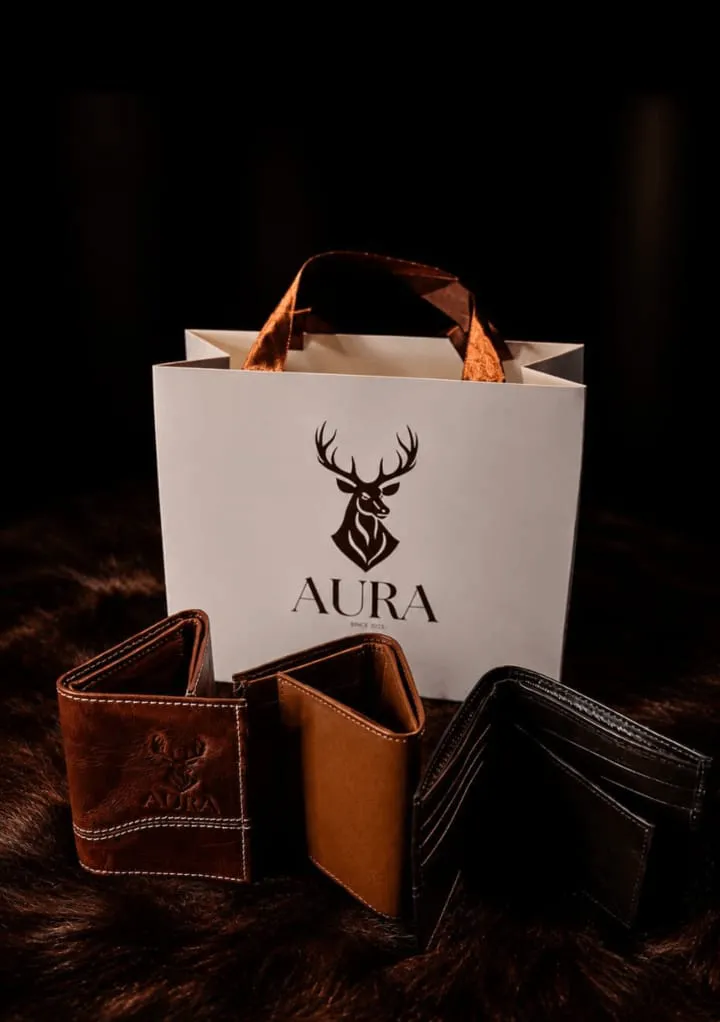 Cartera de cuero AURA sobre fondo claro, junto al empaque de regalo con cinta y tarjeta de cuidado.